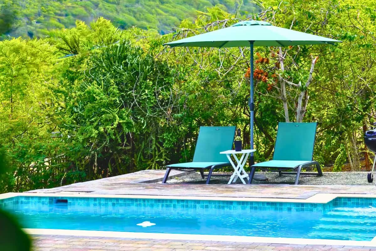 Shared swimming pool with turquoise loungers and an umbrella in a tropical garden