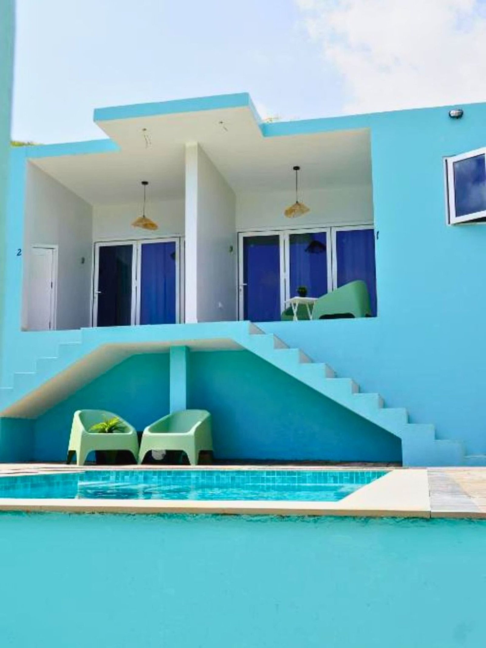 Turquoise studio building with terrace chairs above the shared pool